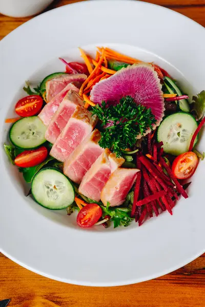 Bir tabak dolusu sebze ve et. Tabak beyaz, sebzeler kırmızı ve yeşil.