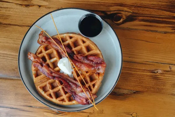 Bir tabak pastırma ve şuruplu waffle. Tabak ahşap bir masanın üzerinde.
