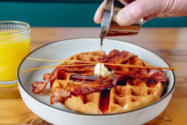 Üzerine şurup dökülmüş bir tabak pastırma ve waffle. Tabak ahşap bir masaya konmuş.