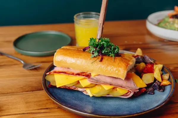 Jambonlu, peynirli ve sebzeli bir sandviç mavi tabakta. Masada bir çatal ve bıçak var.