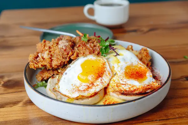 Bir tabak kızarmış tavuk ve yumurta ahşap bir masada oturur. Tabak, kızarmış tavuk, yumurta ve muhtemelen biraz sebze de dahil olmak üzere çeşitli yiyeceklerle dolu. Rahatlık ve hoşgörü kavramı
