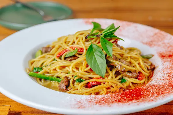 Bir tabak etli ve sebzeli erişte. Erişte kırmızı ve beyaz, et de kahverengi.