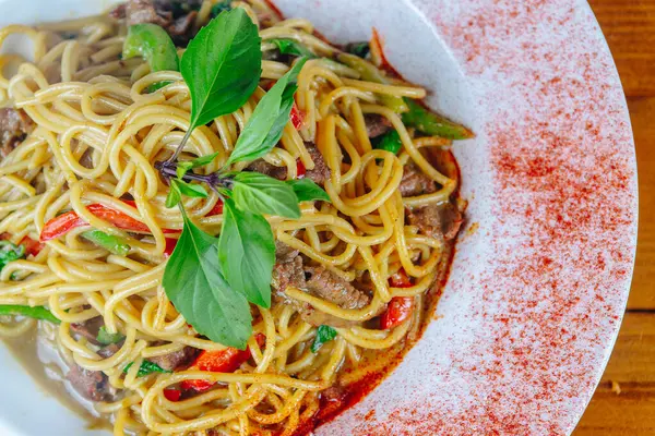A plate of noodles with meat and vegetables. The noodles are long and thin, and the meat is cooked and served on top. The dish is garnished with a sprig of basil, which adds a pop of color