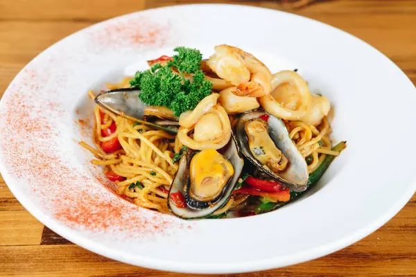 Beyaz plakalı ve kırmızı kenarlı bir tabak yemek. Yiyecekler deniz ürünleri ve sebzelerin karışımı.