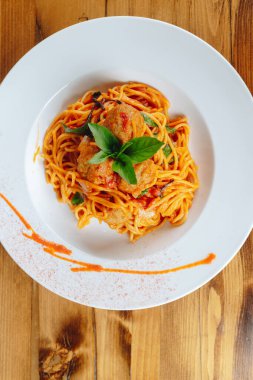 Üstünde köfte ve fesleğen olan bir tabak spagetti. Tabak beyaz, yemek kırmızı.