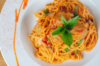 Üstünde köfte ve fesleğen olan bir tabak spagetti. Sos kırmızı ve erişte uzun.