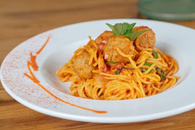 Üstünde köfte ve fesleğen olan bir tabak spagetti. Tabak beyaz, sos kırmızı.