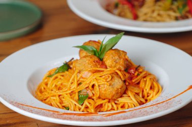 Üstünde köfte ve fesleğen olan bir tabak spagetti. Tabak beyaz, yemek kırmızı.