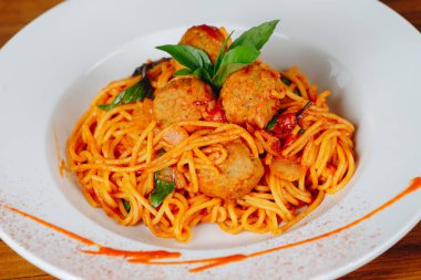 Köfte ve fesleğenli bir tabak spagetti. Tabak beyaz tabakta servis edilir ve üzerine kırmızı sos serpilmiştir.