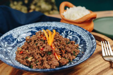 Sebzeli bir kase et ve ahşap bir masada çatal. Kase mavi ve beyaz, çatal da gümüş.