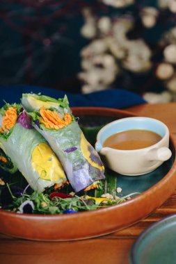 Yanında bir kase sos olan bir tabak yemek. Yemekler sebzeli ve havuçlu rulo.