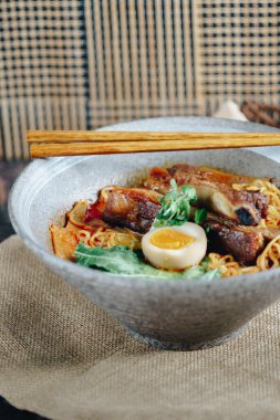 İçinde et ve yumurta olan bir kase ramen. Kase yanında çubuklarla birlikte bir masanın üzerinde.