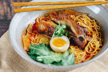 Bir kase etli ve sebzeli erişte. Sebzeler yeşil ve kasede bir parça yumurta var.