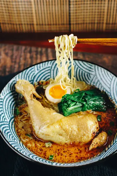 Bir kase çorba, erişte ve tavuk. Tavuk pişti ve yumurta çorbanın içinde yüzüyor. Kase mavi ve beyaz.