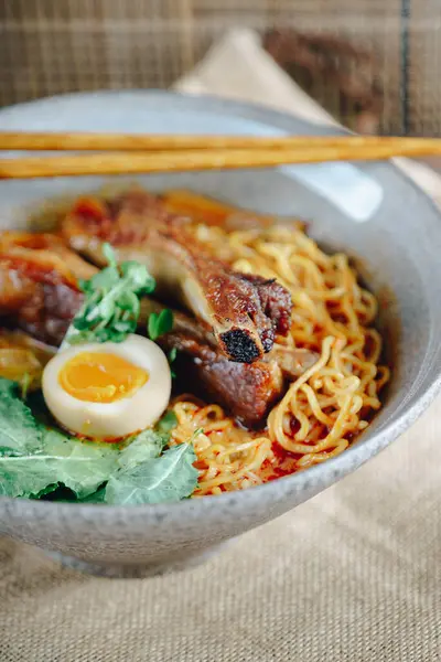 Bir kase et ve yumurtalı erişte. Erişteler uzun ve et küçük parçalara bölünmüş.