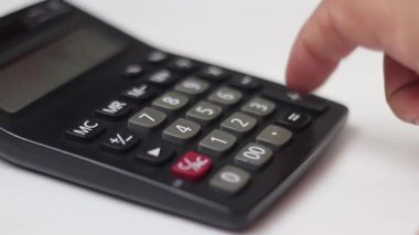 Sayıları hesaplamak için kullanılan siyah hesap makinesi, beyaz arkaplandaki bir parmak tuşuna yakın plan basmak için. Stok videosu.