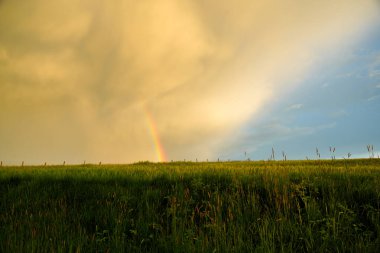 Atmospheric landscape with rainbow, clouds and blue sky and parts of a barb wire fence