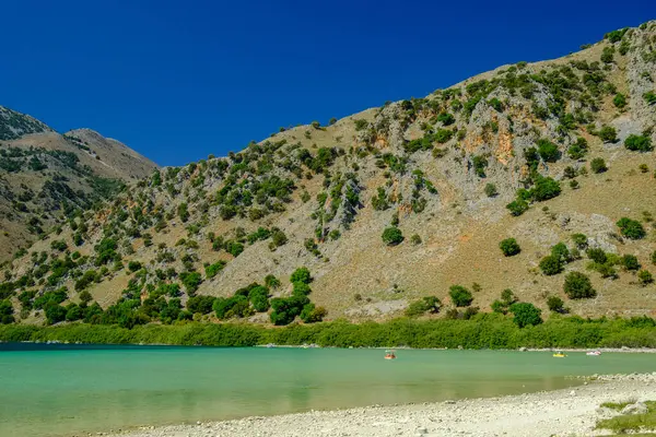 Yunanistan 'ın Girit kentinde mavi gökyüzü altında dağlık manzarayla birlikte Kournas Gölü' nün berrak turkuaz suları