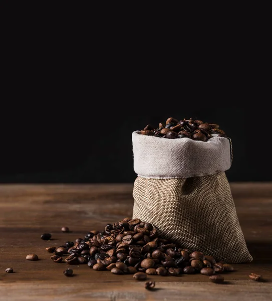 Kahve çekirdekleri ile dolu bir kese kahve dökülmüş kahve çekirdekleri ile kaplı bir masanın üzerinde duruyor.