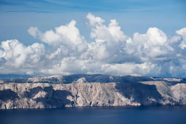 Adanın kayalık uçurumlarından, güneşin doğuşuyla aydınlanan ve ara sıra bulutlarla gölgelenen manzaraya bak..
