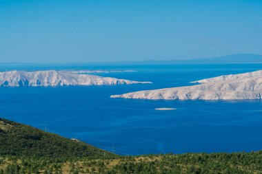 Adanın kayalık uçurumlarından, güneşin doğuşuyla aydınlanan ve ara sıra bulutlarla gölgelenen manzaraya bak..
