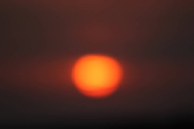 Bulutların ardında saklanan güzel kırmızı bir günbatımı. Güneşin yuvarlak bir silueti.