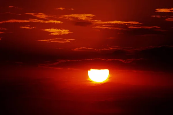 Bulutların ardında saklanan güzel kırmızı bir günbatımı. Güneşin yuvarlak bir silueti.