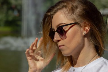 Beautiful blonde on the background of the lake wearing sunglasses and white T-shirt