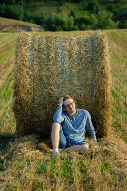 Portrait of a guy with glasses in blue clothes lying on the background of a bale of straw