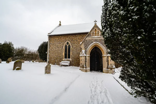 All Saints church in the small village of Sutton in the British countryside, it is totally covered in deep snow during a rare snow storm in the UK