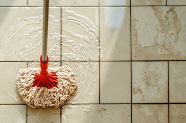 A red mop head cleans a tiled floor clipart