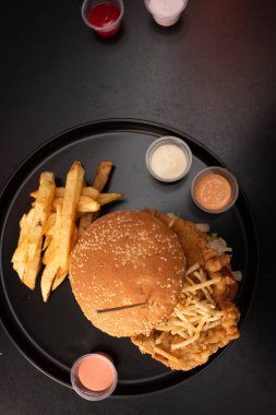 Siyah arka planda kızarmış tavuk burgeri. Domates, marul, tavuk burger, sos ve patates kızartması. Güzel.