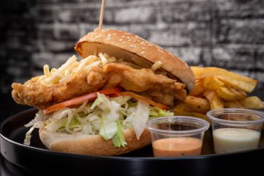 Siyah arka planda kızarmış tavuk burgeri. Domates, marul, tavuk burger, sos ve patates kızartması. Güzel.