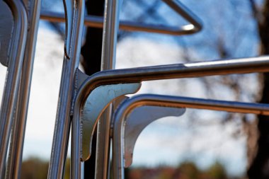 Açık hava yetişkin fitness istasyonundaki metal parmaklıkların ve çerçevelerin detaylı bir yakın çekimi, paslanmaz çelik yapıyı kıvrımlı ve düz elementlerle bulanık doğal bir arka plana karşı gösteriyor.