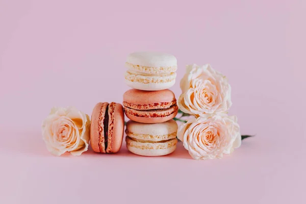 stock image Tasty french macarons with tender rose flowers on a pink pastel background. Place for text.