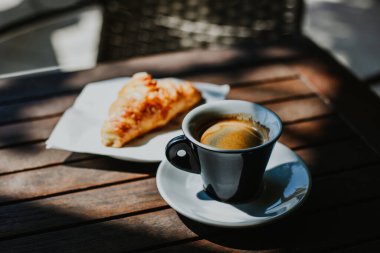 Bir fincan sade kahve ve sokak kafesindeki masada bir kruvasan. Seçici odaklanma. Metin için yer.