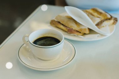 Bir fincan sade kahve ve kafedeki masada bir sandviç. Seçici odak.