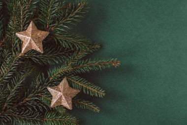 Koyu yeşil arka planda altın parıldayan yıldızlı ladin dalları. Düz yatıyordu. Metin için yer.
