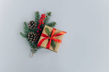 Gri arka planda ladin dalları, koniler ve kırmızı böğürtlenler olan bir hediye kutusu. Tatil konsepti. Metin için yer.