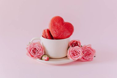Pembe kalp şeklinde, pembe pastel arka planda gül çiçekli Fransız kurabiyeleri. Sevgililer Günü için konsept. Metin için yer.