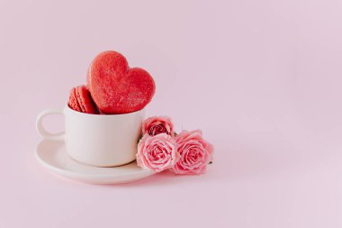 Pembe kalp şeklinde, pembe pastel arka planda gül çiçekli Fransız kurabiyeleri. Sevgililer Günü için konsept. Metin için yer.