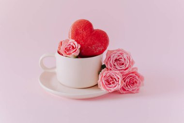 Pembe kalp şeklinde, pembe pastel arka planda gül çiçekli Fransız kurabiyeleri. Sevgililer Günü için konsept. Metin için yer.