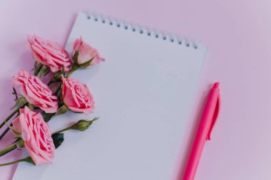 Boş sayfalı bir defter ve pembe arka planda gül çiçekleri. Düz yatıyordu. Metin için yer.