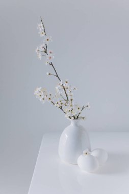 Beyaz çiçekli güzel dallar ve beyaz bir masanın üzerinde yumurtalar. Asgari Paskalya konsepti. Metin için yer.
