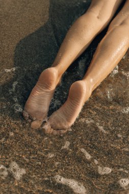 Denizde kadın ayağı. Genç bir kadının sahildeki çıplak ayaklarının yakın plan görüntüsü..