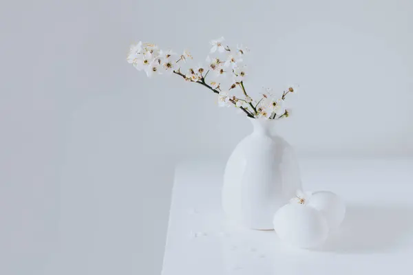 Beautiful blossom branches in a vase and eggs on a white background. Spring minimalistic concept. Place for text.