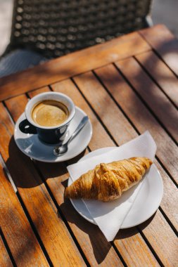 Bir fincan sade kahve ve sokak kafesindeki masada bir kruvasan. Seçici odaklanma. Metin için yer.