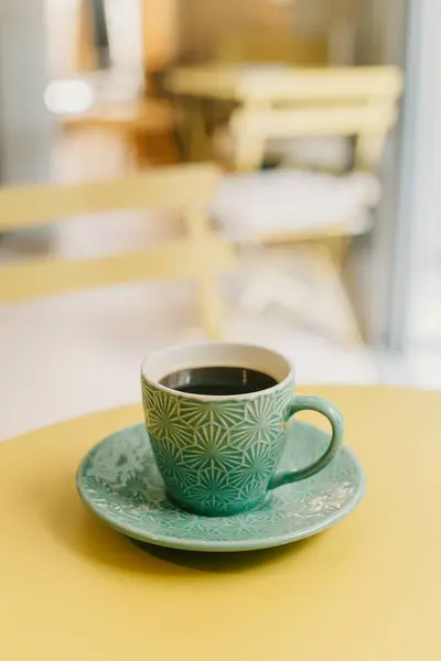 Cup of black coffee in turquoise ceramic cup on a yellow table in a cafe. Place for text.