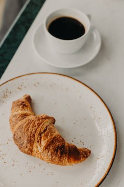 Cup of black coffee and a croissant on a table in a street cafe. Selective focus.