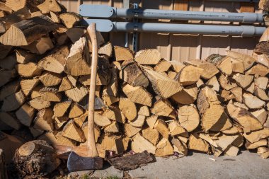 Kesilmiş bir odun yığını ve üzerinde güneş ışıldayan bir duvarın kenarında bir balta.. 